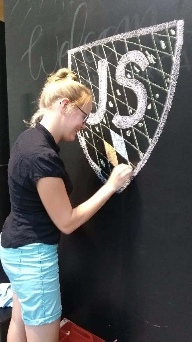 A participant drawing the JSCraftCamp crest in chalk on a blackboard